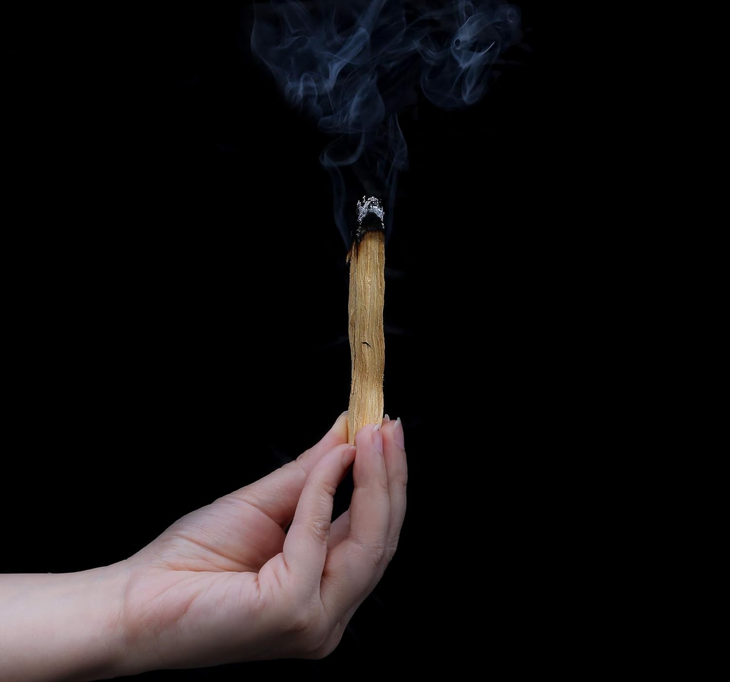 Hand holding a burning match with smoke against a black background