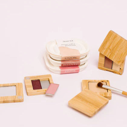 Makeup products including a compact mirror, blush, and a brush on a light background